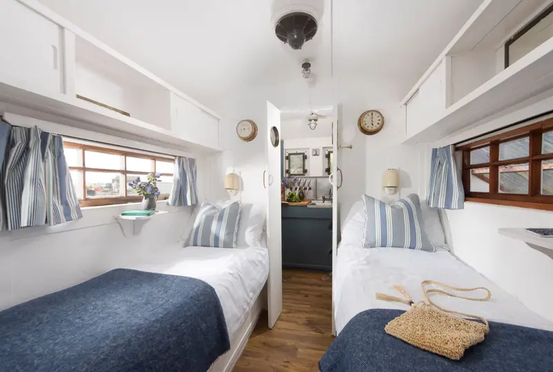 The bedroom, with two single beds made up in white linen and navy throws beneath striped curtains