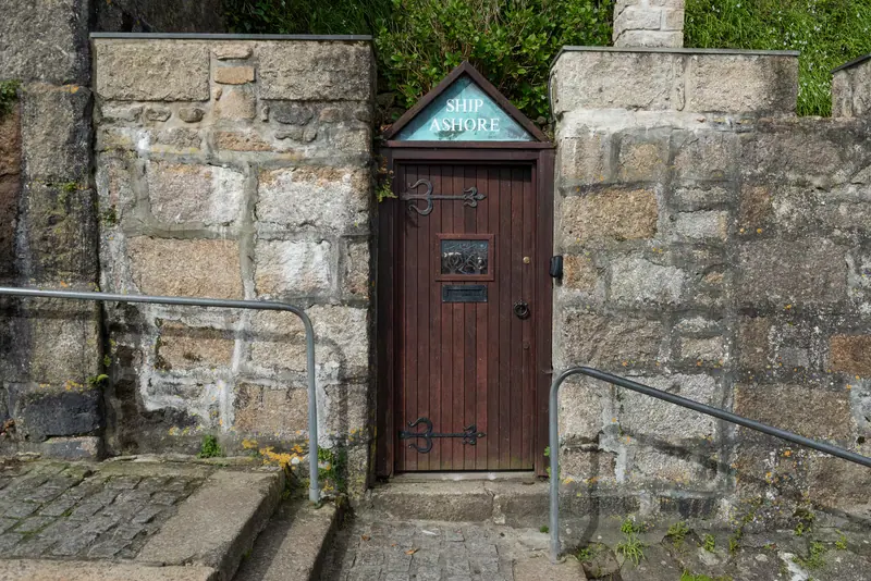 A wooden door set into a granite wall, with a sign above it reading Ship Ashore