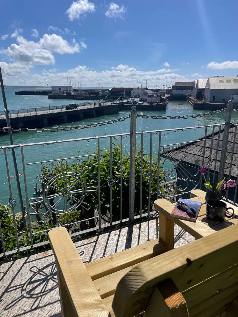 A wooden chair on the terrace looking through the railings to the harbour